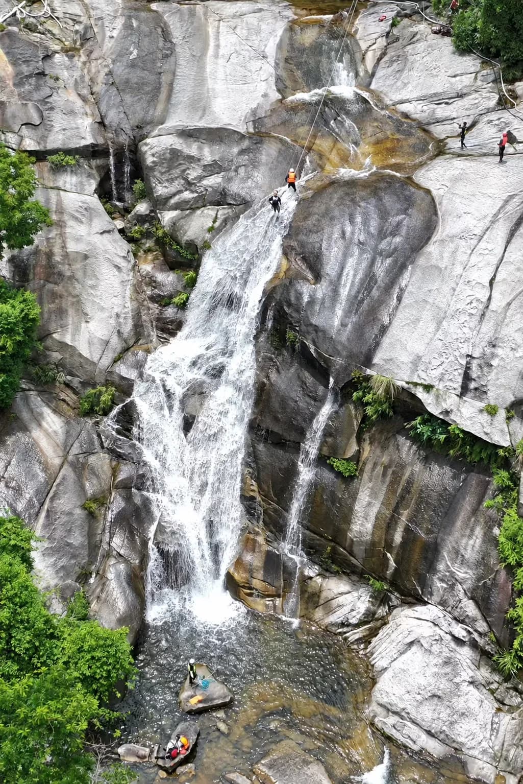 Participants moving with ropes through a broad rainforest waterfall