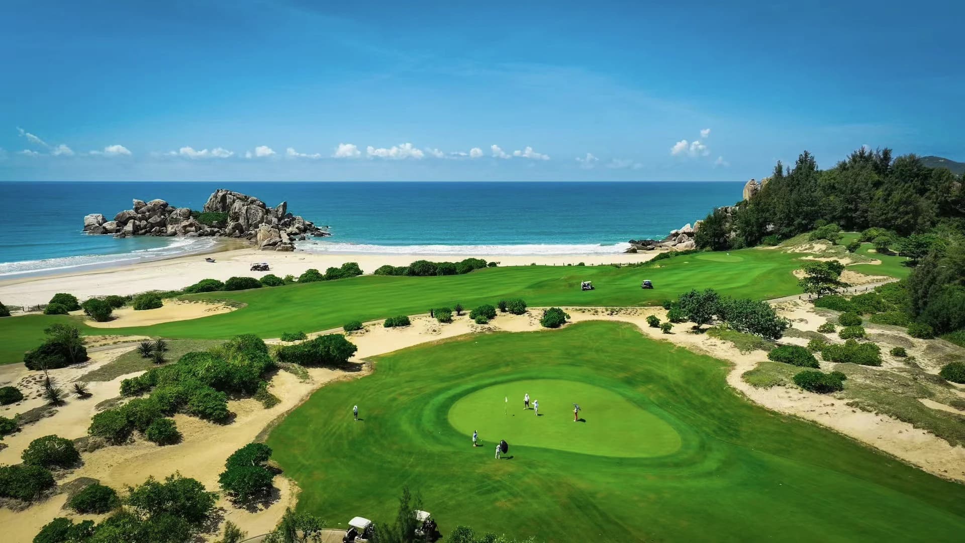 An elevated view across a coastal golf course, beach and open sea