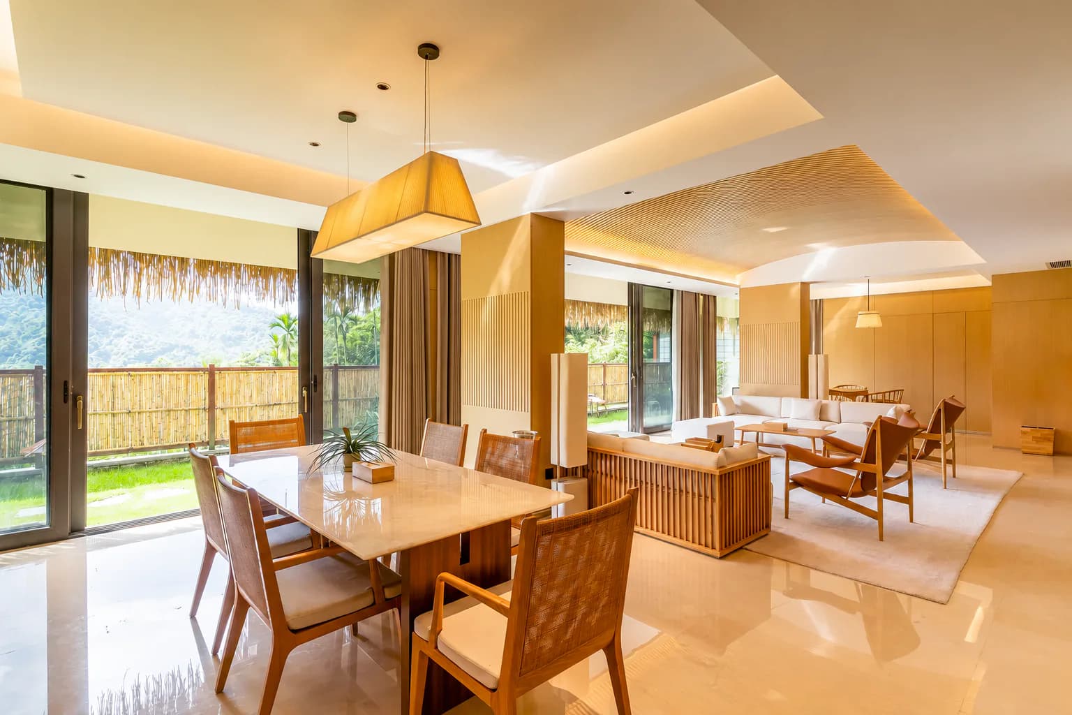 An open shared villa living and dining room looking toward mountain greenery